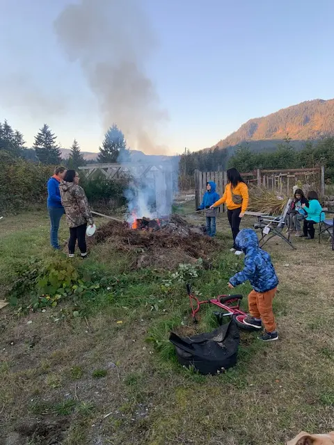 Individuals congregated around a crackling fire in a field, sharing stories and warmth in a serene outdoor setting.