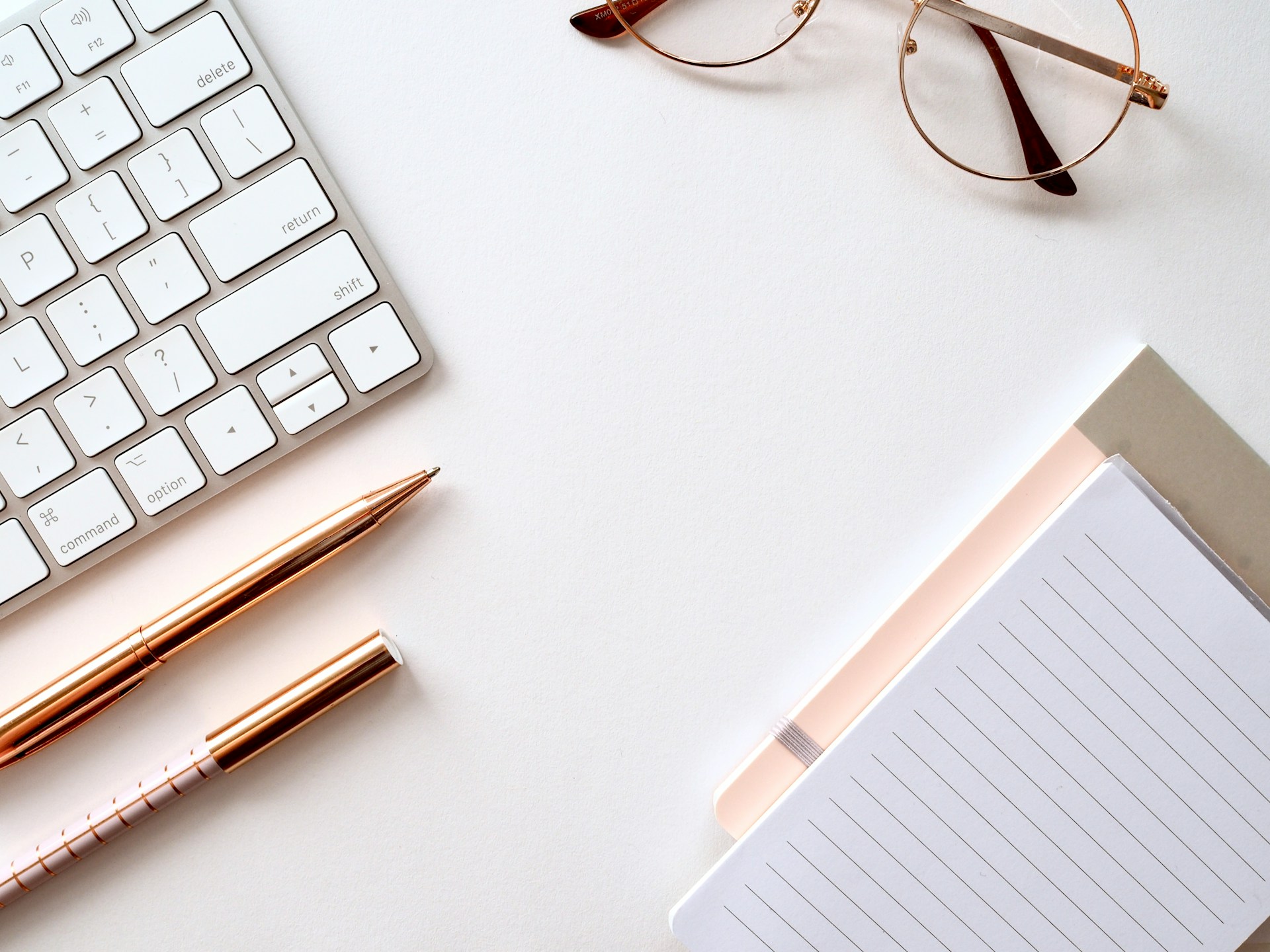 A desk with a keyboard, notebook, pen, and glasses, ready for work or study.